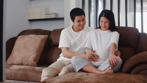 Young Asian Pregnant couple man touch his wife belly talking wit