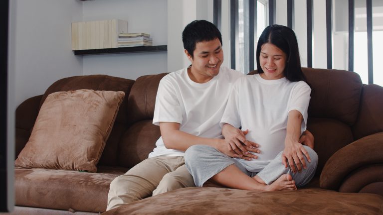 Young Asian Pregnant couple man touch his wife belly talking wit