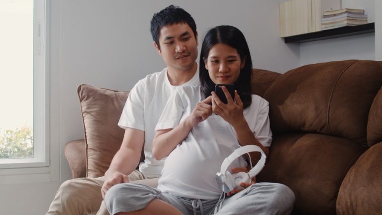 Young Asian Pregnant couple using phone and headphone play music