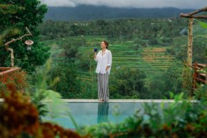 Cheerful elegant woman drinking coffee in the morning near the pool on Bali
