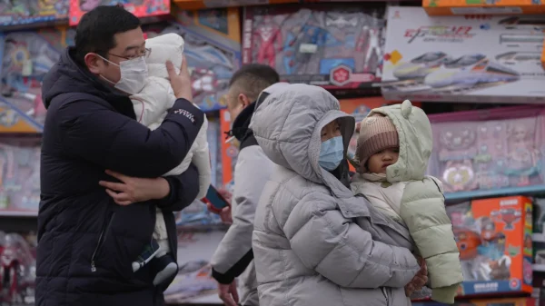 Orang-orang menggendong balita mereka melewati toko mainan di Beijing, Senin, 19 Januari 2026. (AP Photo/Andy Wong)