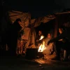 Para pengungsi Palestina menghangatkan diri di sekitar api unggun di sebuah kamp tenda di Kota Gaza, Minggu, 18 Januari 2026. (Foto AP/Jehad Alshrafi)