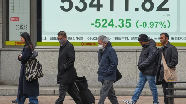 Orang-orang berjalan di depan papan saham elektronik yang menampilkan indeks Nikkei Jepang di sebuah perusahaan sekuritas pada hari Senin, 19 Januari 2026, di Tokyo. (AP Photo/Eugene Hoshiko)