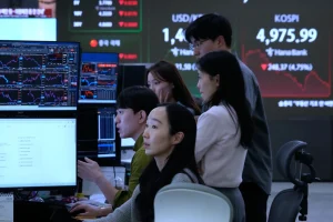 Para pedagang mata uang mengamati monitor di dekat layar yang menampilkan Indeks Harga Saham Komposit Korea (KOSPI), kanan atas, di ruang perdagangan valuta asing kantor pusat Hana Bank di Seoul, Korea Selatan, Senin, 2 Februari 2026. (AP Photo/Ahn Young-joon)