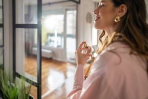 Smiling woman applying perfume in hallway while preparing to go out