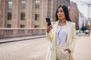 Chinese businesswoman using phone with headphones on the street