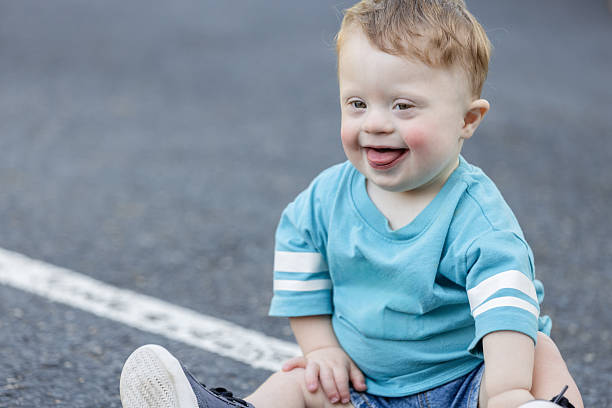Adorable toddler boy with Down Syndrome smiles while playing outdoors
